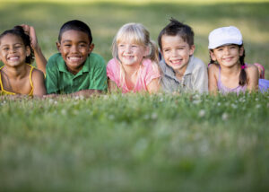 Kinder liegen auf dem Rasen und lachen freundlich in die Kamera