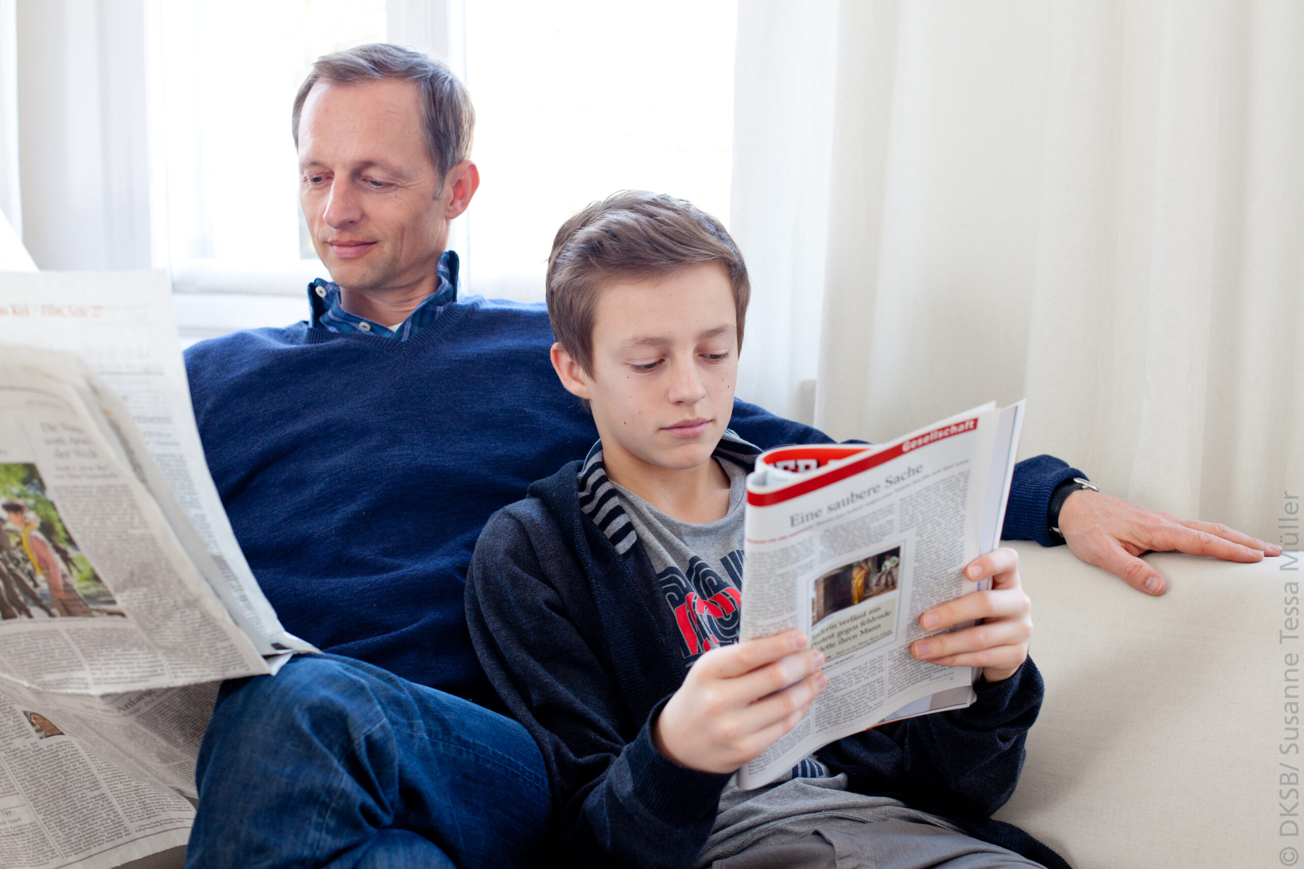 Vater und Sohn sitzen auf der Couch und lesen Zeitung